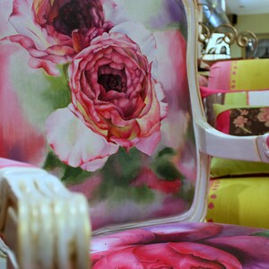 May include: A white and gold armchair with a pink and white floral design. The chair has a high back and a curved armrest. The floral design is a watercolor painting of roses.