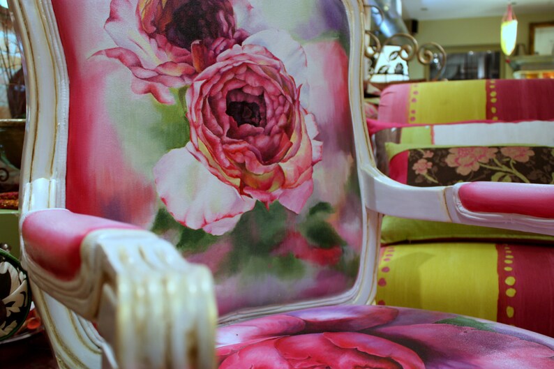 May include: A white and gold armchair with a pink and white floral design. The chair has a high back and a curved armrest. The floral design is a watercolor painting of roses.