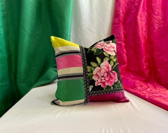 May include: A black and white floral patterned pillow with pink flowers and green, yellow, and pink striped fabric accents. The pillow is sitting on a white surface.