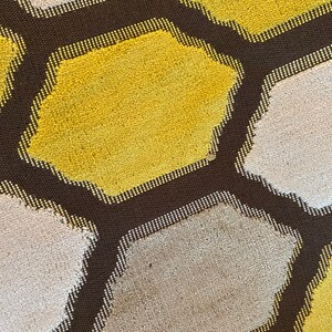 May include: A close-up of a brown, textured fabric with a honeycomb pattern. The hexagons are filled with alternating colors of yellow and white.