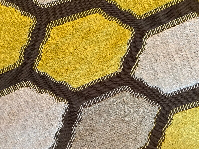 May include: A close-up of a brown, textured fabric with a honeycomb pattern. The hexagons are filled with alternating colors of yellow and white.