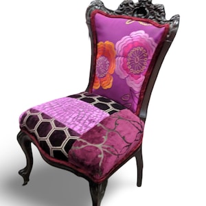 May include: A decorative chair with a dark wood frame and ornate carvings. The backrest features a purple floral pattern, while the seat is a patchwork of various purple fabrics. The chair has curved legs and a red trim.