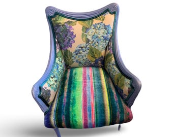 May include: A decorative armchair with a light blue frame. The back and sides feature a floral hydrangea pattern in blue and purple. The seat has a colorful striped design in shades of green, pink, and yellow.