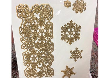 May include: A package of gold-colored snowflake dies in various sizes. The dies are intricate and detailed, perfect for crafting holiday cards and decorations. The package is on a white background.