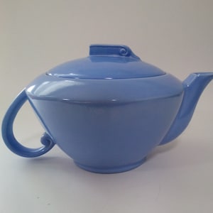 May include: A light blue ceramic teapot with a lid and a curved handle. The teapot has a simple, elegant design.