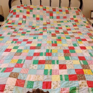 May include: A patchwork quilt in a variety of colors, including red, green, yellow, and blue, covers a bed. The quilt is made of numerous fabric squares, creating a vibrant and textured pattern. The bed frame is dark brown.