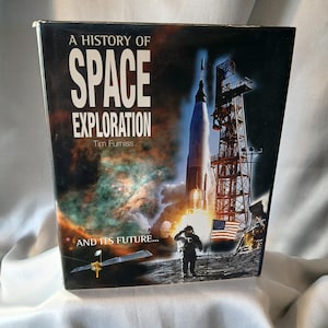May include: A book titled "A History of Space Exploration" by Tim Furniss. The cover features a rocket launching, an astronaut saluting, and a satellite. The background shows a nebula and the American flag.