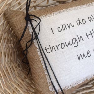 May include: A burlap pillow with a white linen panel featuring the text "I can do all things through Him who strengthens me". The pillow has black twine ties.
