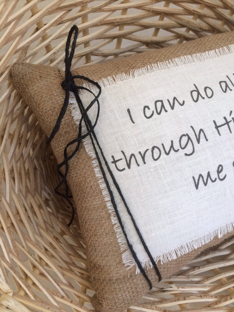 May include: A burlap pillow with a white linen panel featuring the text "I can do all things through Him who strengthens me". The pillow has black twine ties.