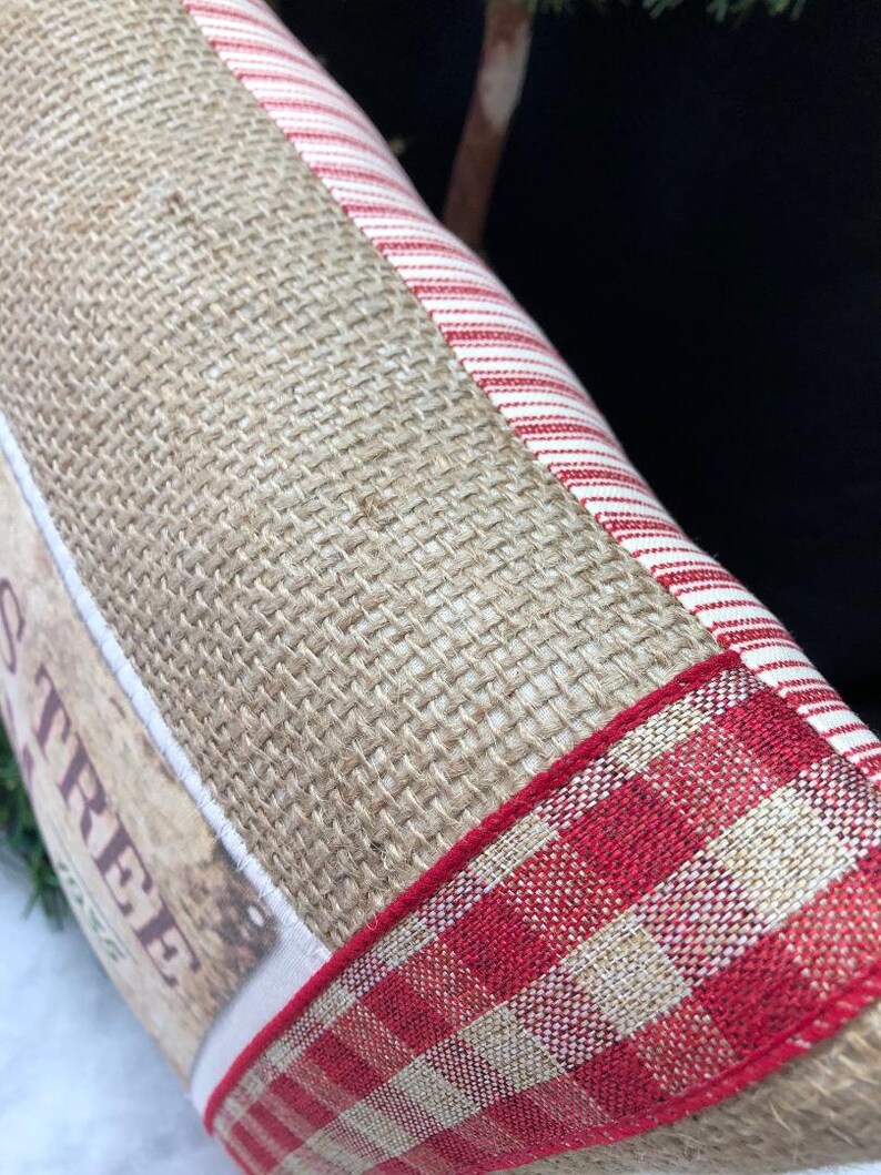 May include: A burlap pillow with a red and white striped fabric panel and a red and white gingham ribbon trim. The pillow has a vintage-style label that says "Christmas Tree".
