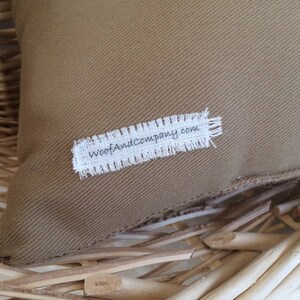 May include: A brown canvas pillow with a white label that says "WoofAndCompany.com" on it.