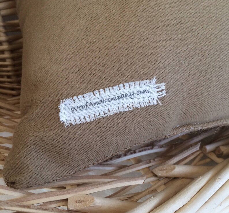May include: A brown canvas pillow with a white label that says "WoofAndCompany.com" on it.