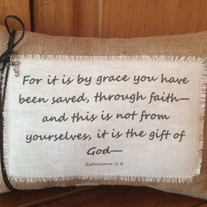 May include: A burlap pillow with a white fabric insert featuring the Bible verse "For it is by grace you have been saved, through faith - and this is not from yourselves, it is the gift of God - Ephesians 2:8".
