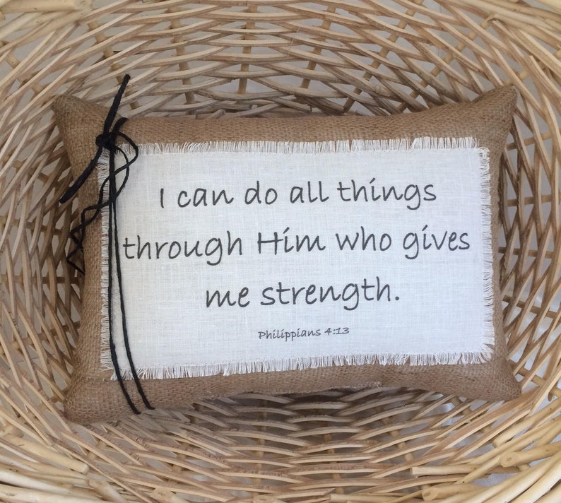 May include: A burlap pillow with a white fabric insert featuring the quote "I can do all things through Him who gives me strength. Philippians 4:13".