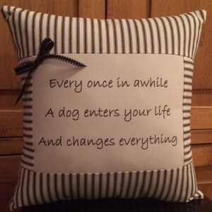 May include: A white and black striped pillow with a white fabric panel featuring the text "Every once in awhile A dog enters your life And changes everything".