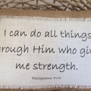 May include: A white fabric pillow with a black embroidered quote: "I can do all things through Him who gives me strength. Philippians 4:13".