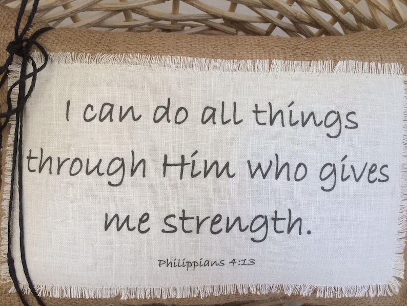 May include: A white fabric pillow with a black embroidered quote: "I can do all things through Him who gives me strength. Philippians 4:13".