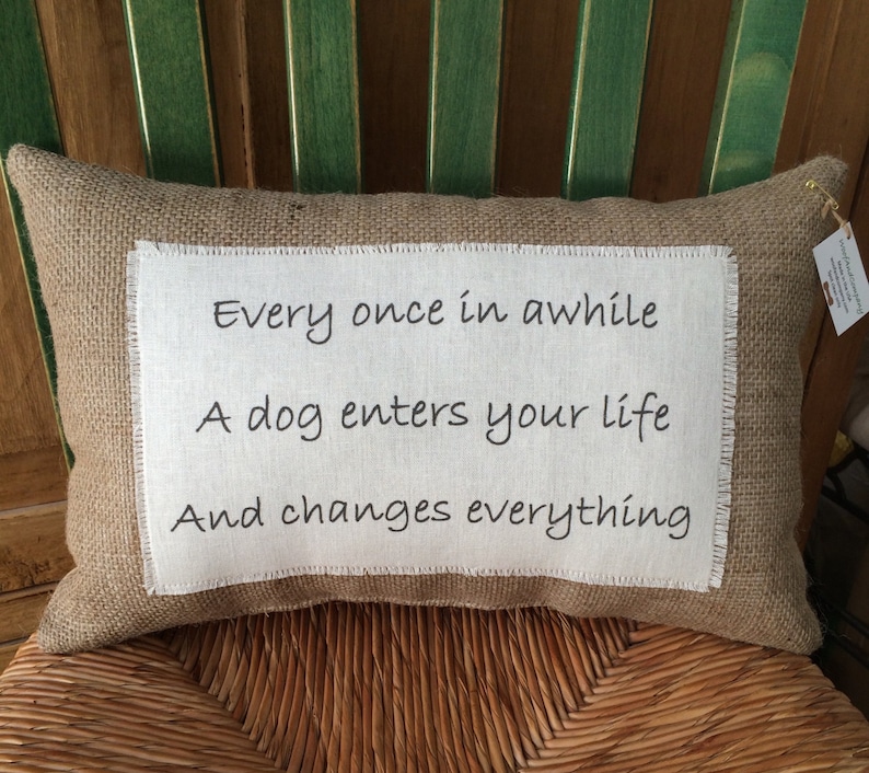 May include: A burlap pillow with white fabric insert featuring the text "Every once in awhile A dog enters your life And changes everything".