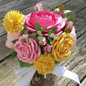 May include: A bouquet of paper flowers in a glass jar. The flowers are pink, yellow, and green. The jar is filled with small rocks.