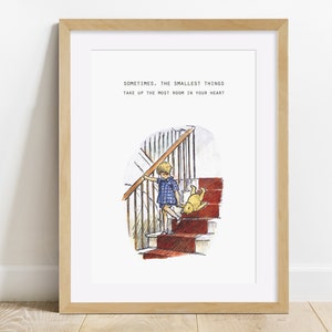 Puede incluir: Una impresi&oacute;n enmarcada con una cita de Winnie de Pooh: "A veces, las cosas m&aacute;s peque&ntilde;as ocupan el mayor espacio en tu coraz&oacute;n." La impresi&oacute;n presenta una ilustraci&oacute;n de acuarela de un ni&ntilde;o subiendo una escalera con un oso de peluche.