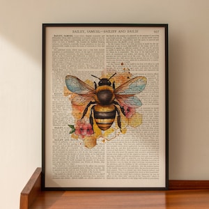 May include: Framed art print featuring a detailed illustration of a bee with outstretched wings, set against a backdrop of vintage book pages. The bee is in shades of brown, yellow, and black, with a honeycomb and floral design. The print is in a black frame.