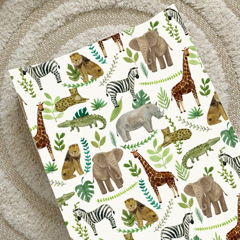 K&ouml;nnte beinhalten: Ein wei&szlig;er Hintergrund mit einem sich wiederholenden Muster aus Dschungeltieren und Pflanzen. Zu den Tieren geh&ouml;ren Giraffen, Elefanten, Zebras, L&ouml;wen, Nash&ouml;rner und Krokodile. Die Pflanzen sind gr&uuml;n und belaubt.