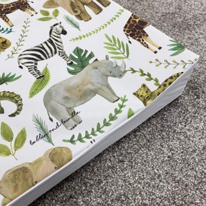 K&ouml;nnte beinhalten: Wei&szlig;e Spielmatte mit einem Dschungeltier-Druck. Die Matte zeigt ein Zebra, ein Nashorn, eine Giraffe, einen Elefanten, einen Leopard und ein Krokodil. Der Text "babblin and bumble" ist auf der Matte gedruckt.