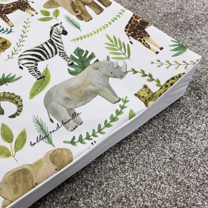 K&ouml;nnte beinhalten: Wei&szlig;e Spielmatte mit einem Dschungeltier-Druck. Die Matte zeigt ein Zebra, ein Nashorn, eine Giraffe, einen Elefanten, einen Leopard und ein Krokodil. Der Text "babblin and bumble" ist auf der Matte gedruckt.