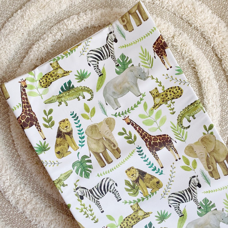 K&ouml;nnte beinhalten: Wei&szlig;er Stoff mit einem sich wiederholenden Muster aus verschiedenen Tieren, darunter Zebras, Giraffen, Elefanten und Nash&ouml;rner. Die Tiere sind im Cartoon-Stil mit gr&uuml;nem Laub und Bl&auml;ttern illustriert.