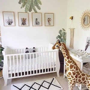 K&ouml;nnte beinhalten: Ein wei&szlig;es Babybett mit einer wei&szlig;en und schwarzen gemusterten Matratze, einem Stofftier-Giraffe und einer Wickelkommode mit einer wei&szlig;en und schwarzen gemusterten Wickelauflage. Das Zimmer ist im Dschungel-Stil eingerichtet, mit gr&uuml;ner und brauner Tiermuster-Tapete und gerahmten Tierdrucken an der Wand.