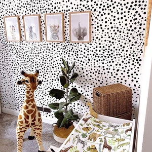K&ouml;nnte beinhalten: Eine wei&szlig;e Wickelauflage mit einem schwarz-wei&szlig;en Tiermuster. Die Wickelauflage liegt auf einem wei&szlig;en Wickeltisch mit einem Stofftier in Form einer Giraffe auf dem Boden daneben. Die Wand hinter dem Wickeltisch ist mit schwarzen und wei&szlig;en Punkten bedeckt.