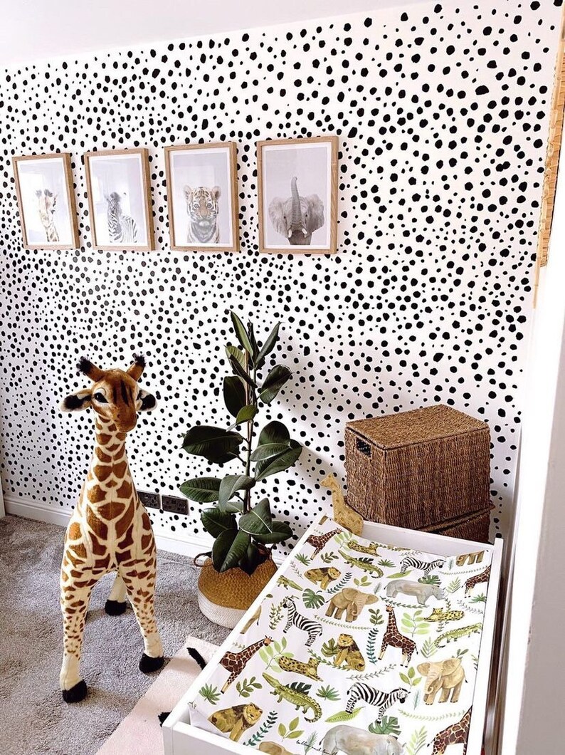 K&ouml;nnte beinhalten: Eine wei&szlig;e Wickelauflage mit einem schwarz-wei&szlig;en Tiermuster. Die Wickelauflage liegt auf einem wei&szlig;en Wickeltisch mit einem Stofftier in Form einer Giraffe auf dem Boden daneben. Die Wand hinter dem Wickeltisch ist mit schwarzen und wei&szlig;en Punkten bedeckt.