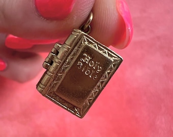 Può includere: Un ciondolo color oro a forma di libro, con le parole "Holy Bible" incise sulla copertina. Il ciondolo ha un design dettagliato, tra cui il dorso e le pagine. Il ciondolo è sospeso da un piccolo anello.