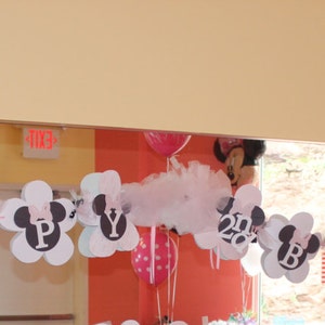 May include: A white and black banner with the word "Happy" and Mickey Mouse ears, decorated with white tulle and pink and red balloons.