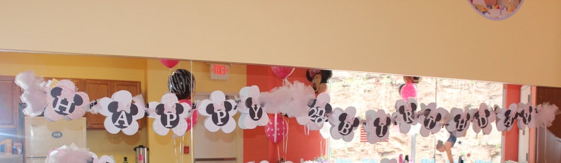 May include: A white and black banner with the word "Happy" and Mickey Mouse ears, decorated with white tulle and pink and red balloons.