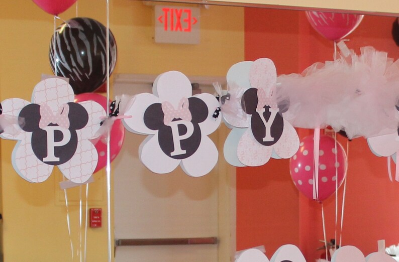 May include: A pink and white banner with the letters "HAPPY" spelled out in black letters. Each letter is on a white flower-shaped card with a black Mickey Mouse silhouette and a pink bow. The banner is hanging from the ceiling with pink and white balloons.