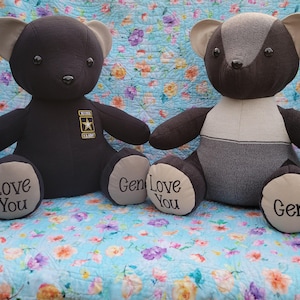 May include: Two plush teddy bears made from fabric. The left bear is solid black with a U.S. Army patch on its chest and the words Love You and Gene embroidered on its light-colored foot pads. The right bear is multi-toned gray and black.