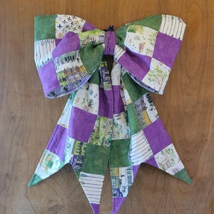 Könnte beinhalten: Eine große, dekorative Schleife aus Patchwork-Stoff in Lila, Grün und Weiß. Die Schleife weist eine Vielzahl von Mustern auf, darunter florale, geometrische und architektonische Designs. Die Schleife wird wahrscheinlich zur Dekoration verwendet.