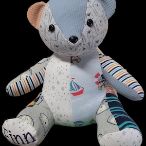 May include: A handmade patchwork teddy bear with a variety of patterned fabrics. The bear features a blue corduroy head, patterned ears, and a mix of fabrics with bear, nautical, and star designs. The name "Finn" is embroidered on one foot.