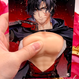 May include: A rectangular print featuring a male anime character with black hair and blue eyes, wearing a black cloak and red vest. The print is held by a hand, with a flesh-toned object in front of the character's chest. The background includes pink rose petals and a gold frame.