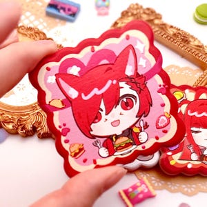 Könnte beinhalten: Ein roter und rosa Aufkleber mit einer Cartoon-Figur mit roten Haaren und Fuchsohren, die einen Burger und eine Gabel hält. Der Aufkleber hat einen gewellten Rand und ist von rosa und roten Akzenten umgeben. Weitere Aufkleber und dekorative Elemente befinden sich im Hintergrund.