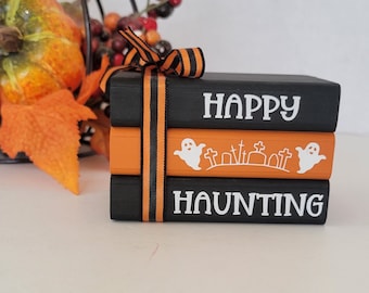 May include: A stack of three black and orange wooden blocks with the words "Happy Haunting" in white lettering. The blocks are tied together with a black and orange ribbon.