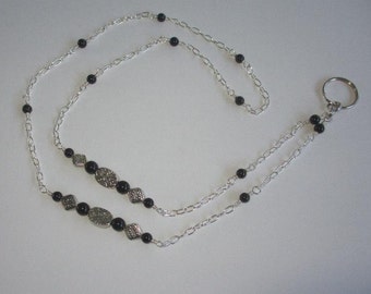 May include: A silver chain with black beads and a silver key ring. The chain is double-stranded and has a decorative design on the beads.