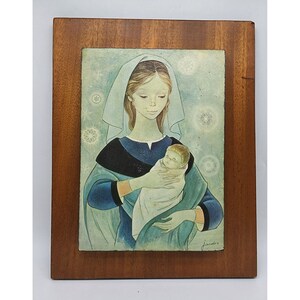May include: A framed painting of a woman holding a baby. The woman is wearing a blue robe and a white veil. The baby is wrapped in a white cloth. The background is a light blue with snowflakes.
