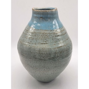 May include: A light blue and gray ceramic vase with a rounded body and a wide opening. The vase has a speckled glaze and a smooth, glossy finish.