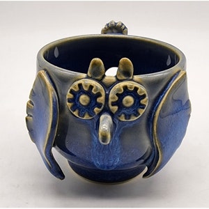 May include: A blue ceramic owl-shaped bowl with yellow accents. The bowl has two large eyes and a beak.