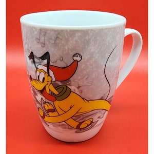 May include: White ceramic mug featuring Pluto from Disney, wearing a Santa hat and ice skating. The mug has a winter theme with musical notes and snowflakes on a gray background. The mug has a white handle.