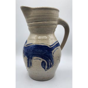 May include: A stoneware pitcher with a blue and white design of a dog. The pitcher has a handle and a rounded body.