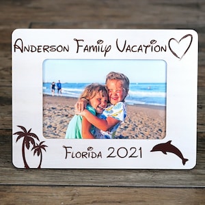May include: White wooden photo frame with a brown heart, palm trees, and a dolphin. The frame has the text "Anderson Family Vacation Florida 2021" and a photo of two girls on a beach.
