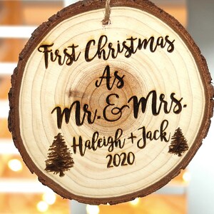 May include: A round wooden ornament with the text "First Christmas as Mr. & Mrs. Haleigh + Jack 2020" and two small pine tree illustrations.